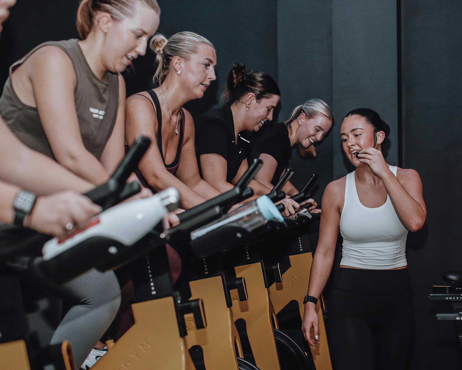 A photo of a group women and their trainer during a spin class. 